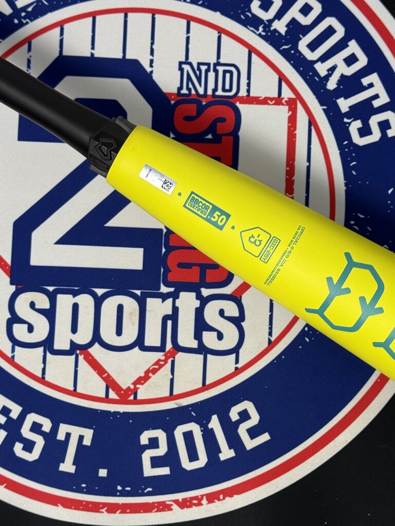 Close-up of yellow baseball bat barrel with teal emblem and small stamped markings